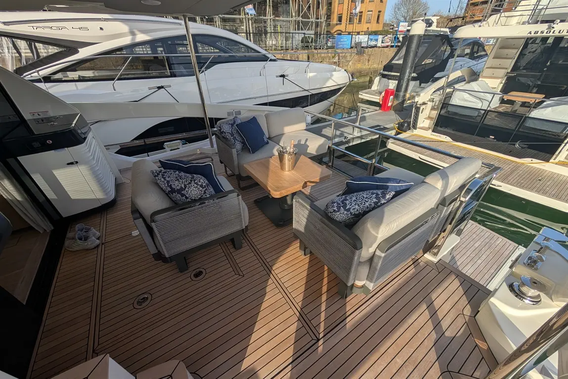 Luxury yacht deck with stylish seating, a table, and a champagne bucket, overlooking docked motorboats in a marina.